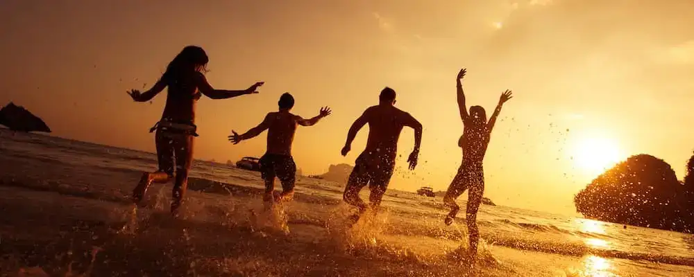 friends jumping into the water sunset