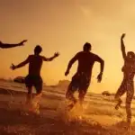 friends jumping into the water sunset