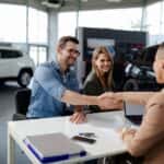man shaking hands with a sales person while his wife sits next to him