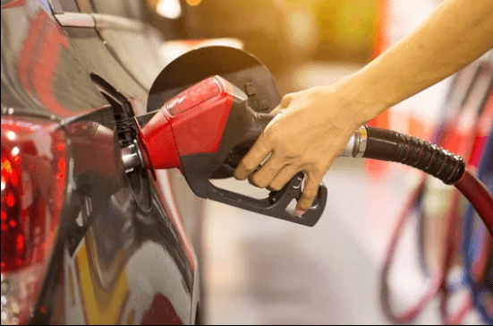 a hand holding a red gas pump filling up the gas tank of a black vehicle