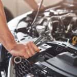 person with wrenches and other tools looking under the hood of a vehicle