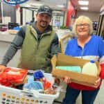 Customers of CarHop of Tulsa smiling with their Thanksgiving gift baskets, including a turkey and other holiday essentials.