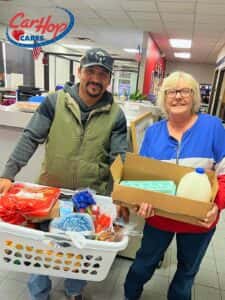 Customers of CarHop of Tulsa smiling with their Thanksgiving gift baskets, including a turkey and other holiday essentials.