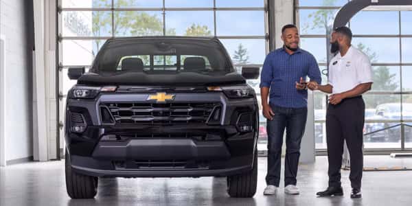 Chevrolet customer and Service Advisor standing next to a Chevrolet Colorado pickup in a Chevy Express Service drive. Service your vehicle at Castle Chevrolet Of Mchenry McHenry, your Chevy Service Center near Rockford, IL.