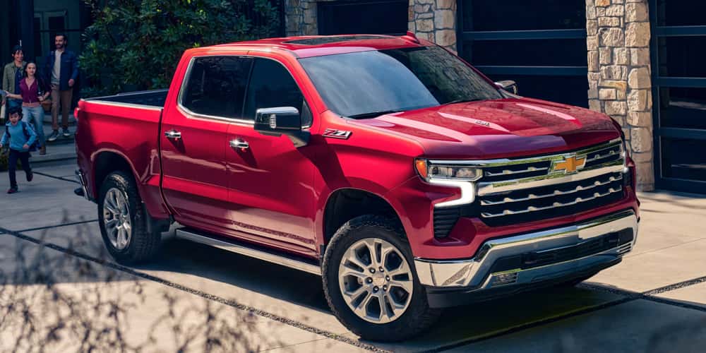 Red Chevrolet Silverado 1500 pickup shown in the driveway of a luxury home. Visit Castle Chevrolet Of Mchenry McHenry, your Chevy dealer near Rockford, IL.