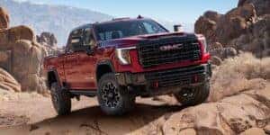 2025 GMC Sierra 3500 AT4X in red navigating rocky terrain in a desert mountain landscape, highlighting off-road performance and rugged design.