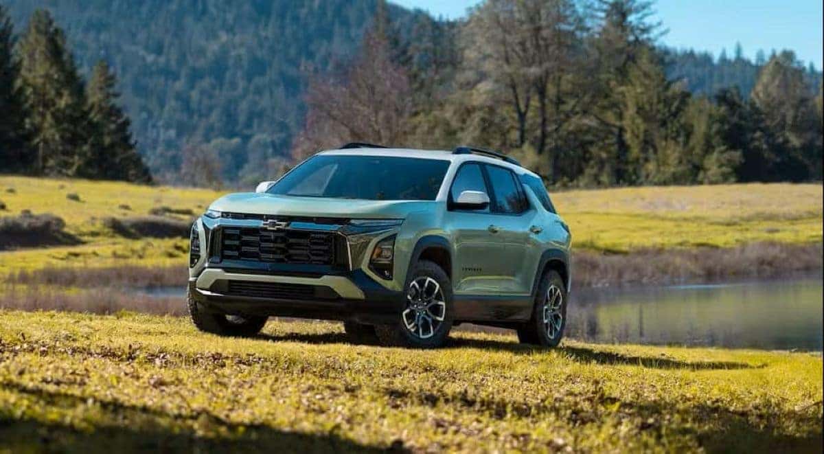 2026 Chevrolet Equinox parked in a grassy field near a pond with forested hills in the background, highlighting its rugged yet modern design.