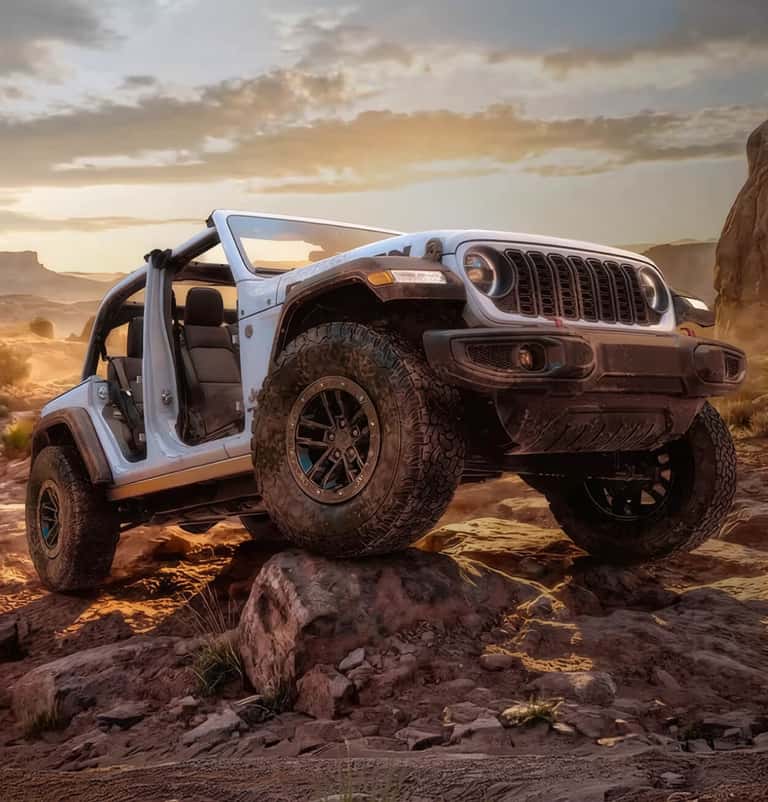 Three-quarter front view of an open-top, doorless white Jeep Wrangler Rubicon scaling rugged rocks.