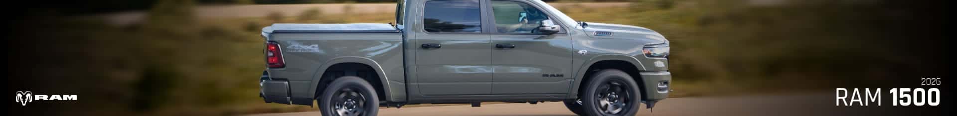 Side view of a gray Ram 1500 driving on a road and with a natural landscape in the background.