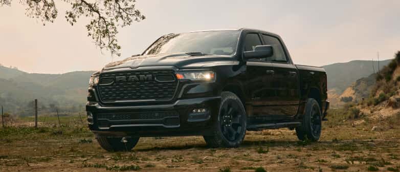 Low front three-quarter view of a black RAM 1500 parked on a dirt field near hills.