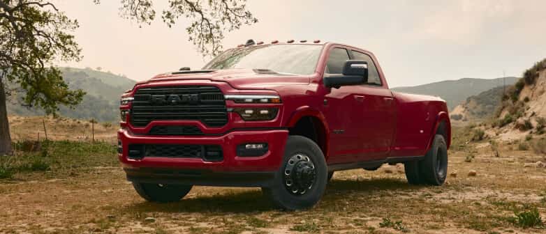 Low front three-quarter view of a red RAM 3500 parked on a dirt field near hills.