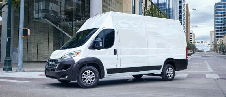 Front three-quarter view of a white RAM ProMaster cargo van parked on a city street.