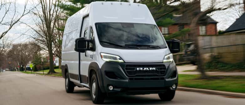 Front view of a white RAM ProMaster EV delivery van driving down a suburban residential street.