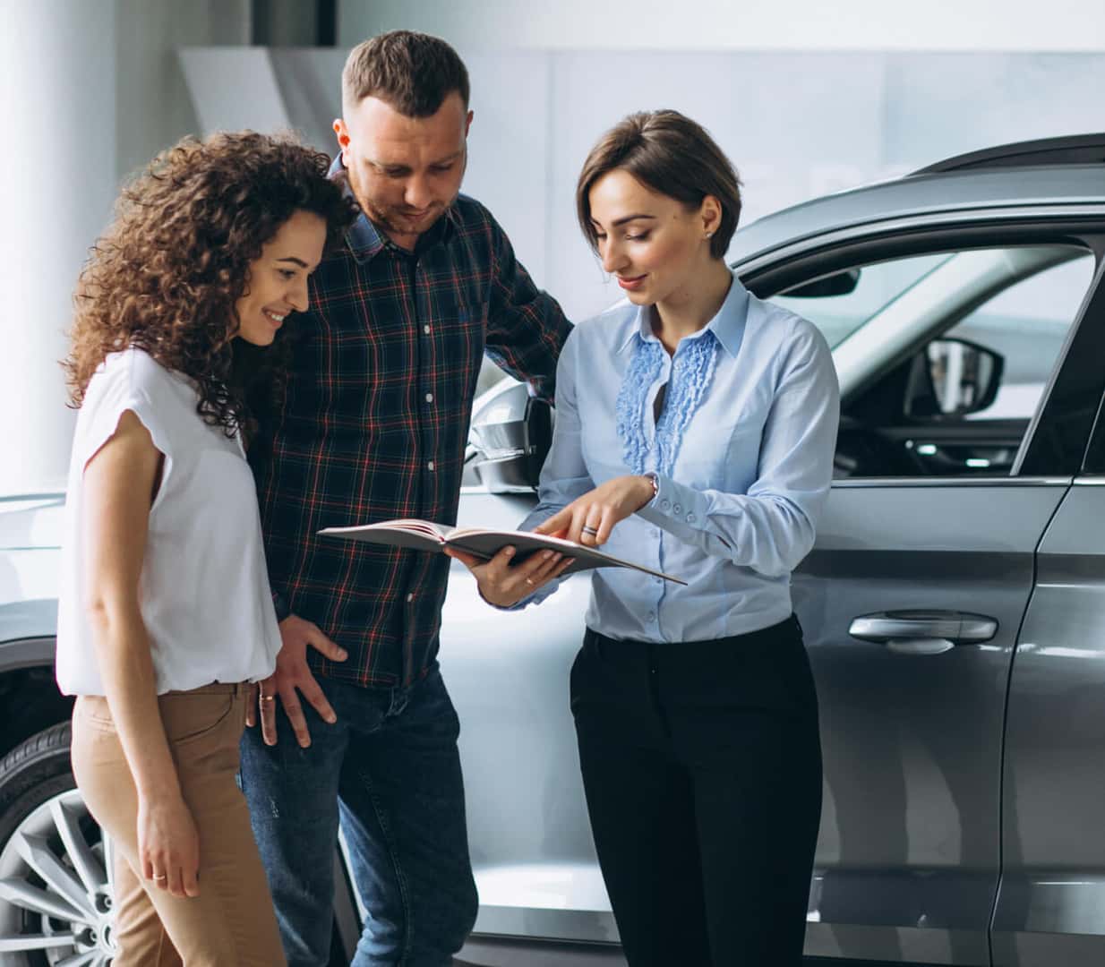 A sales associate points to a brochure book while a smiling pair of customers follows along.