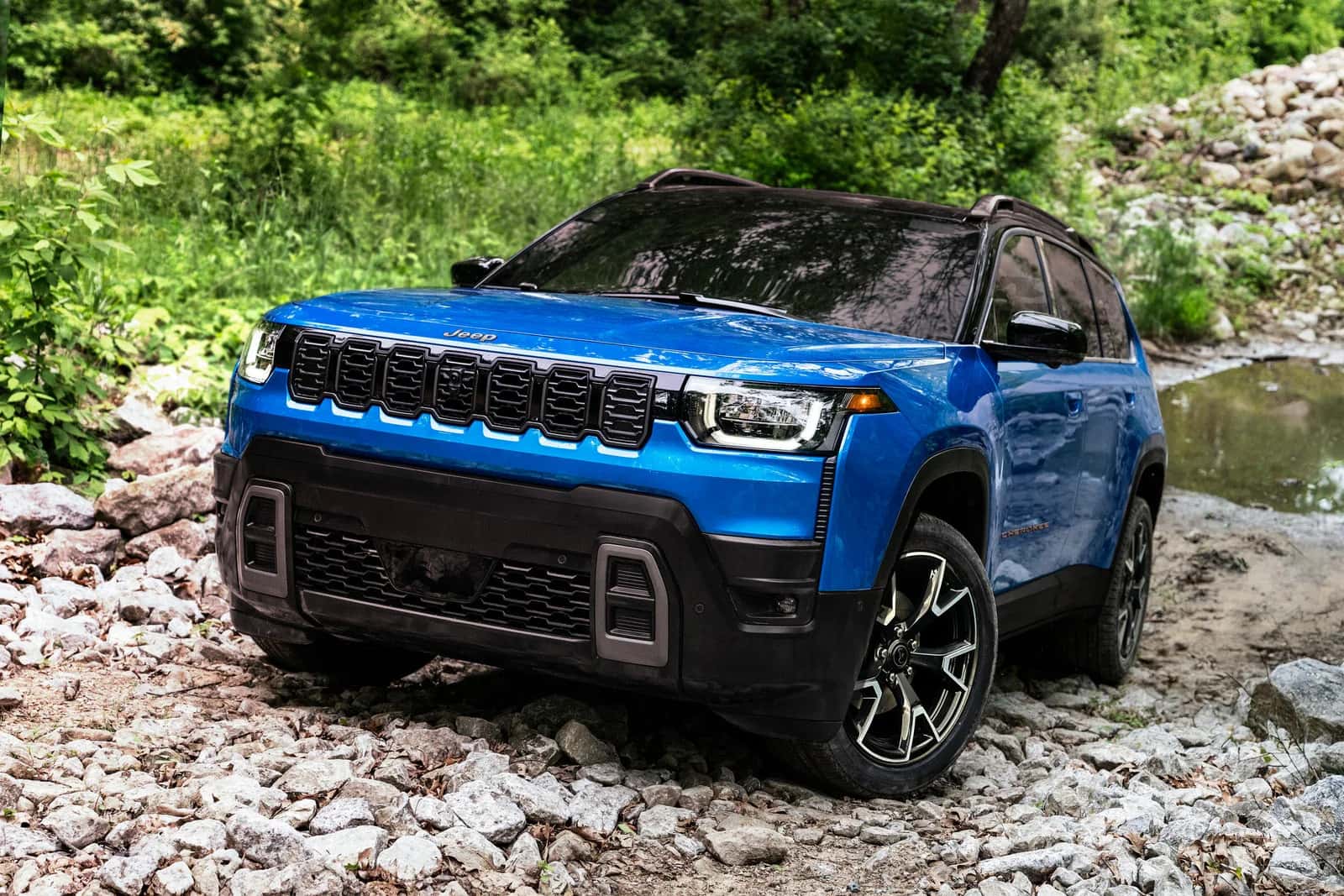 a blue 2026 jeep cherokee driving over a rocky terrain in the woods