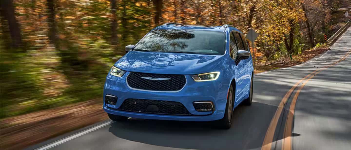 blue 2026 pacifica plug in hybrid drivign down a winding road in the woods
