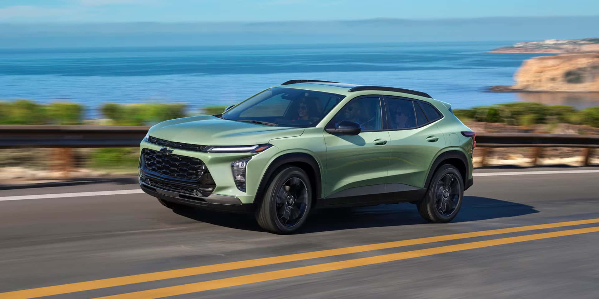 a green 2026 chevy trax driving on the highway near water