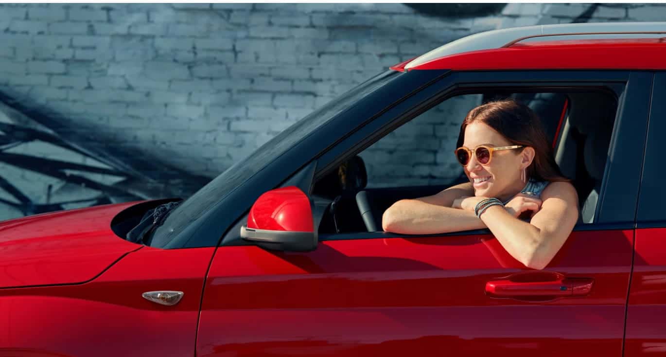 Woman in sunglasses enjoys driving a red car with a brick wall mural background.
