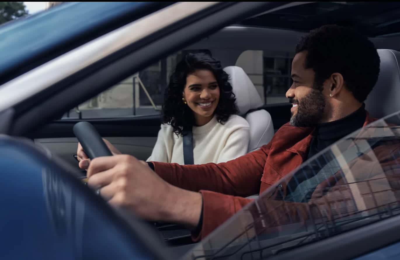 Driver and front passenger smiling at each other inside a Hyundai Tucson.