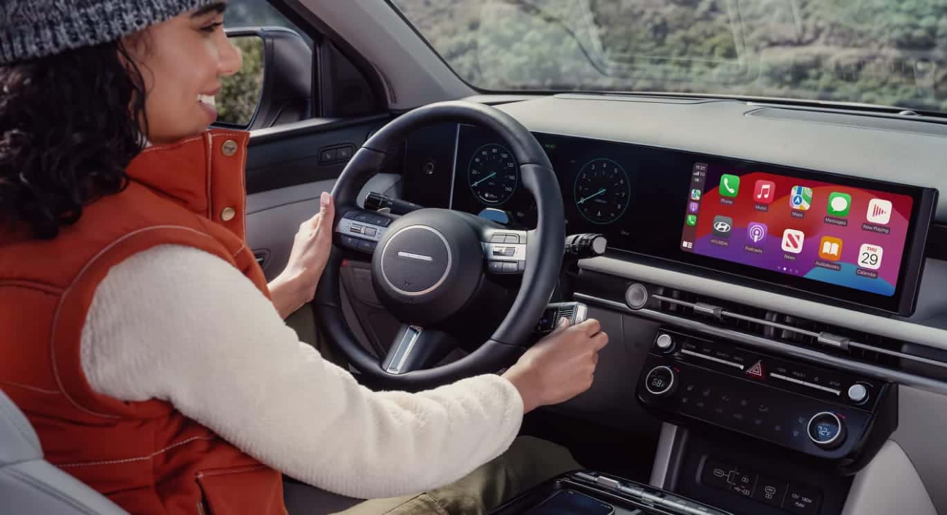 Driver inside a Hyundai Tucson using the dashboard touchscreen with Apple CarPlay displayed.