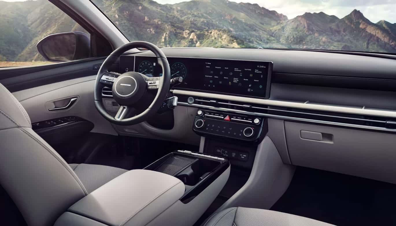 Hyundai Tucson interior featuring the steering wheel, panoramic digital display, center console, and light-colored seating.