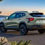 2026 Chevrolet Trax parked by a scenic waterfront at sunset, showing rear design, black wheels, and compact SUV styling