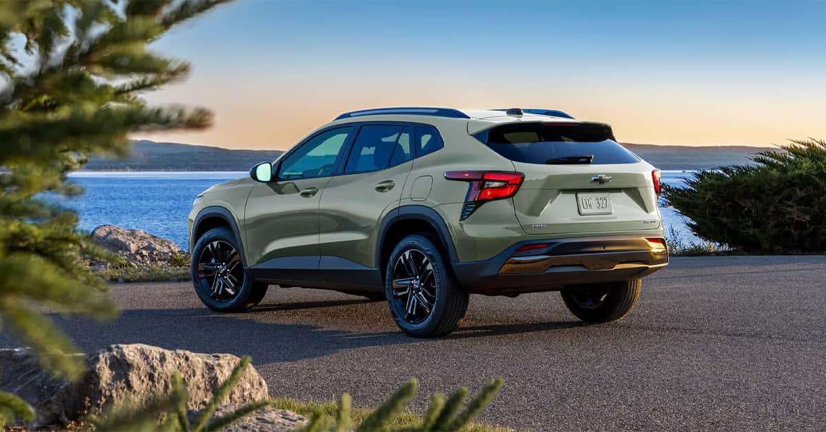 2026 Chevrolet Trax parked by a scenic waterfront at sunset, showing rear design, black wheels, and compact SUV styling