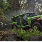 Green 2026 Jeep Wrangler Rubicon with doors removed parked near a stream in a forest.