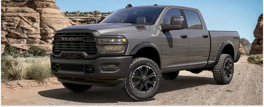 Front three-quarter view of a dark grey 2026 RAM 2500 pickup truck on a desert dirt road.