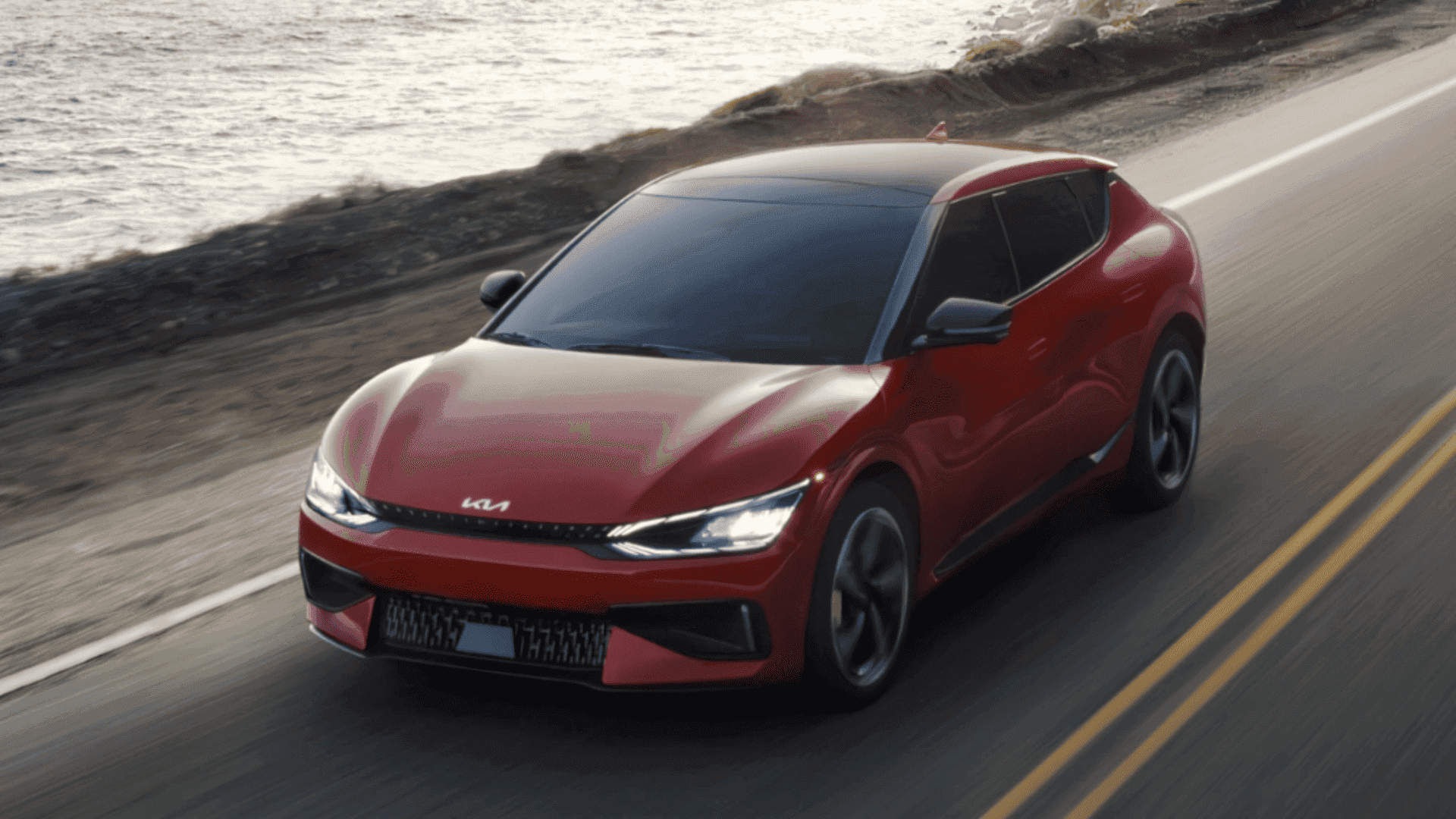 Red 2024 Kia EV6 driving along a coastal highway under evening light