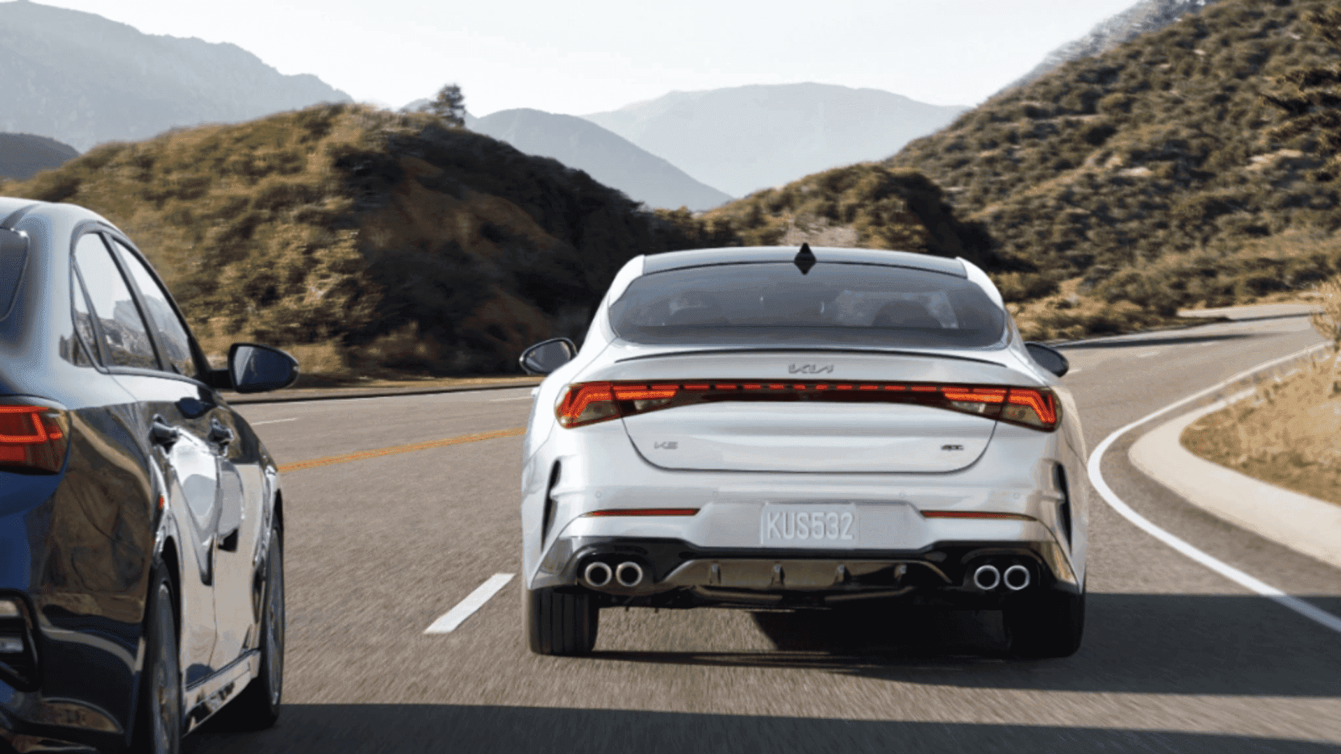Rear view of the 2024 Kia K5 driving along a scenic mountain road