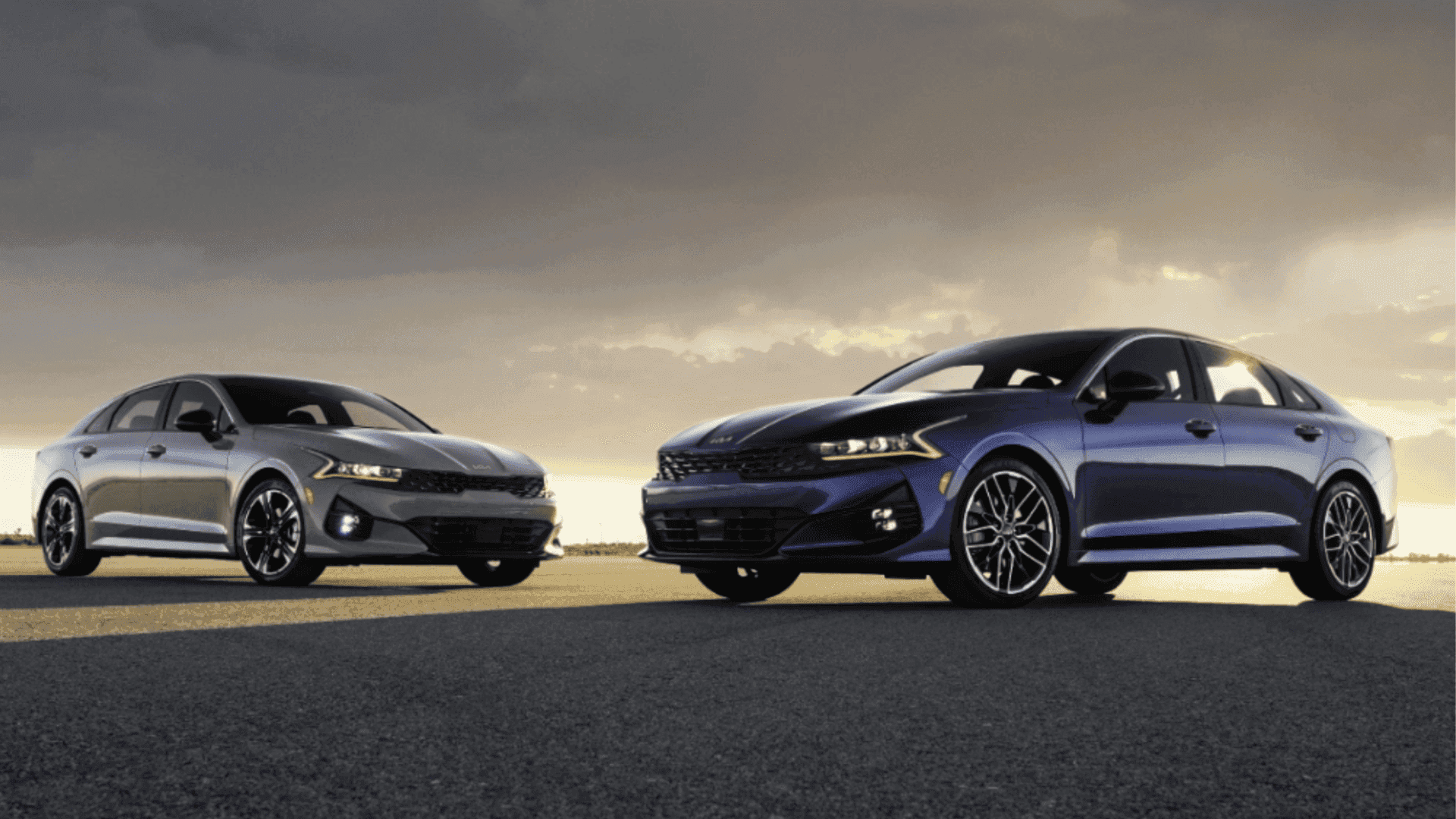 Silver and blue 2024 Kia K5 sedans parked side-by-side at sunset.