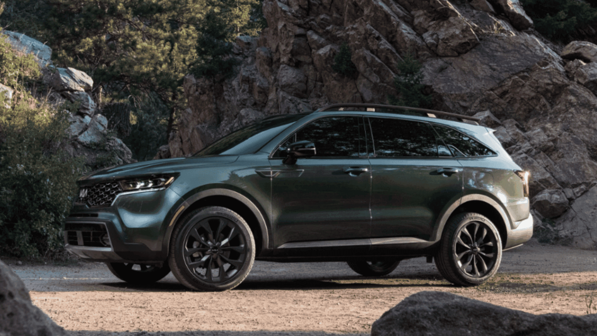 Green 2024 Kia Sorento SUV parked near rocky terrain and trees.