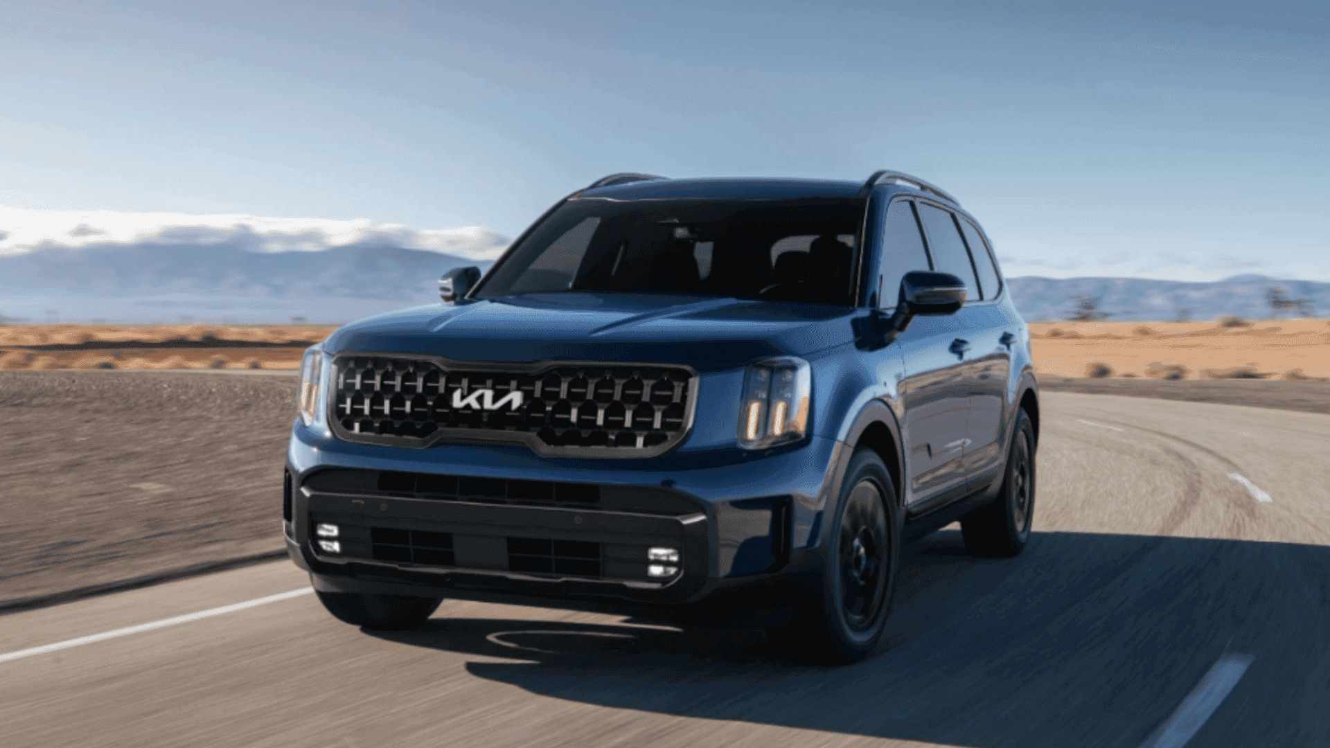 Blue 2024 Kia Telluride SUV driving along a desert highway.