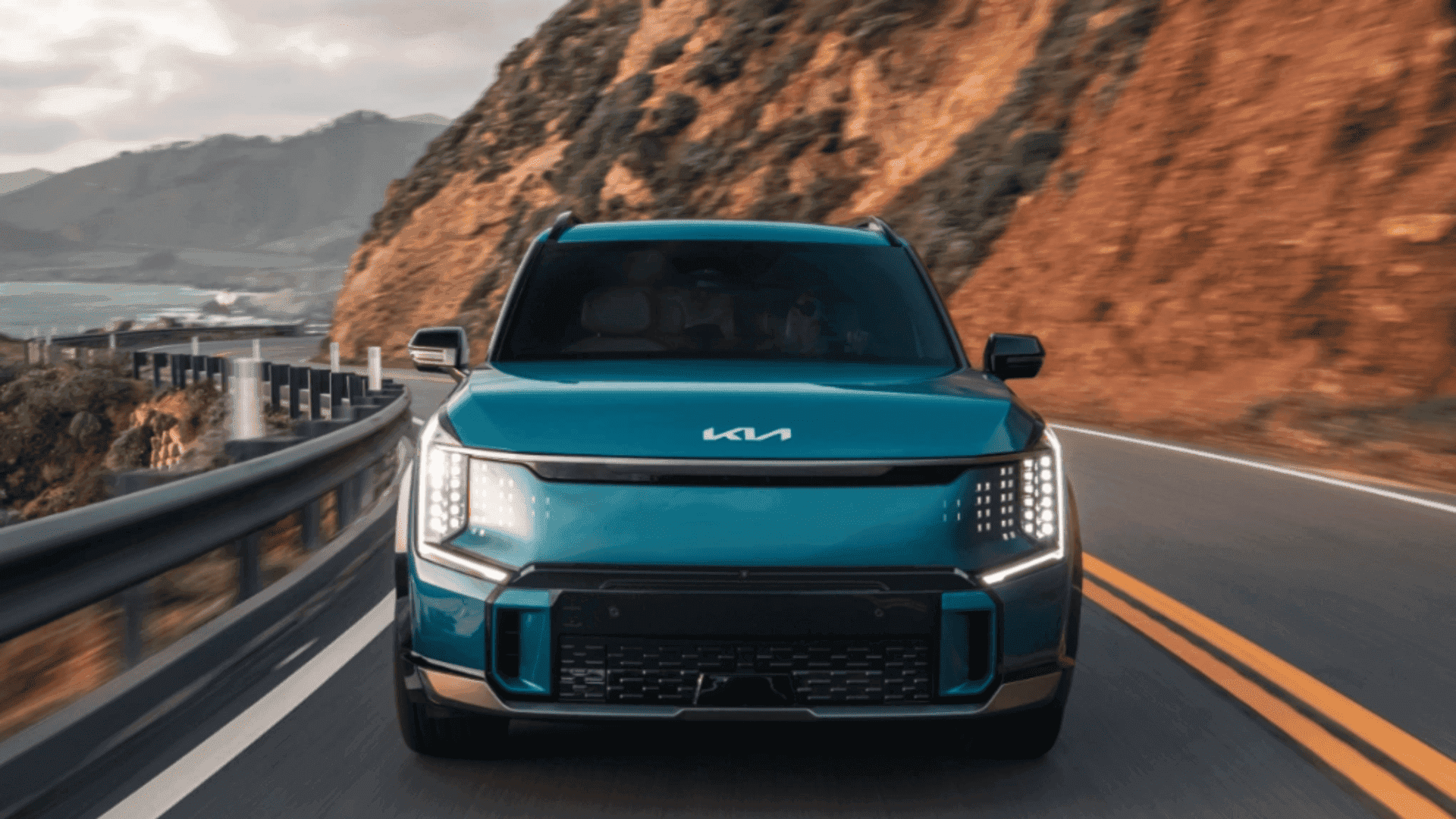 Front view of blue 2024 Kia EV9 driving on a coastal highway