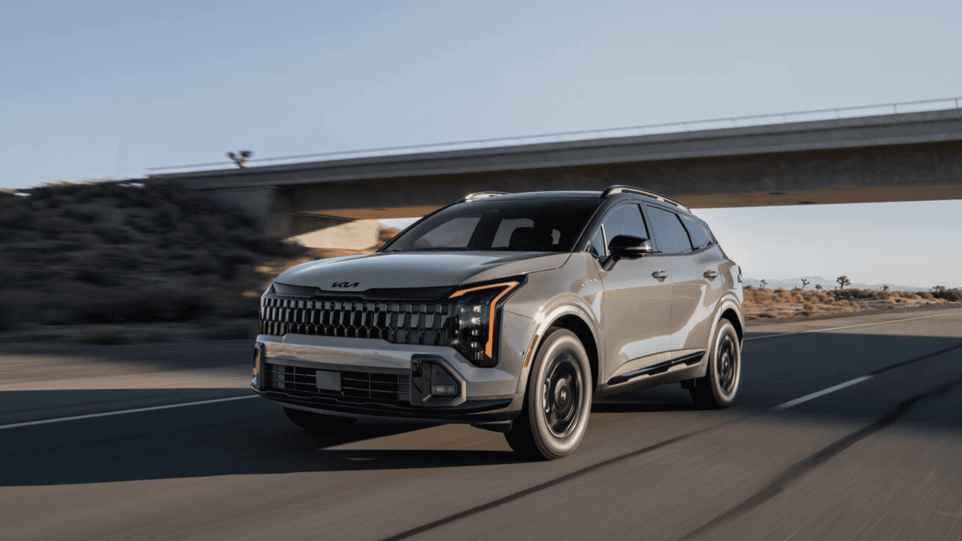 2026 Kia Sportage SUV driving on highway under overpass with modern headlights and bold grille.