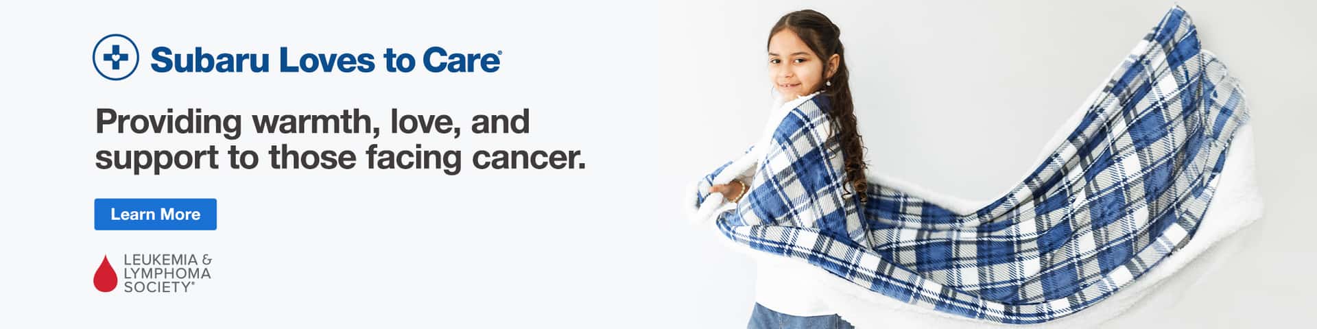 Subaru Loves to Care. Young girl smiling wrapped in blue flannel blanket.