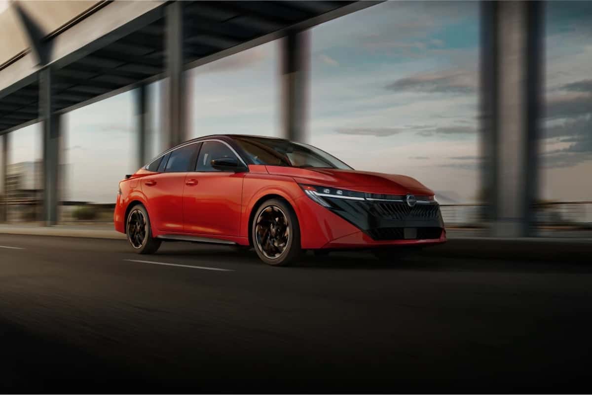 Red Nissan sedan driving on a highway, blurred background