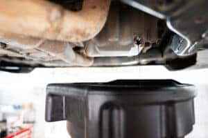 Close-up view of engine oil draining from a car into a pan. 