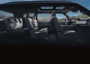Side profile view of the 2025 Nissan Armada interior showcasing three rows of black leather seats with contrast stitching, a panoramic sunroof, and a high-tech dashboard with digital displays, set against a scenic mountain backdrop through the windows.