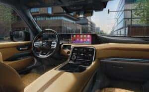 Interior view of the 2025 Nissan Armada featuring a luxurious tan leather cabin, quilted seats, a digital instrument cluster, and a wide infotainment screen displaying Apple CarPlay, set against a cityscape visible through the windshield.