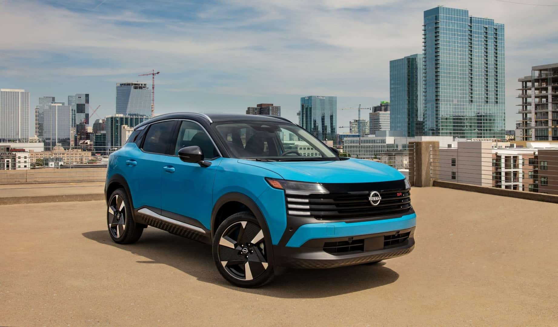 The Pretty Blue 2024 Nissan Kicks, Parked In Front Of An Expansive City Scape