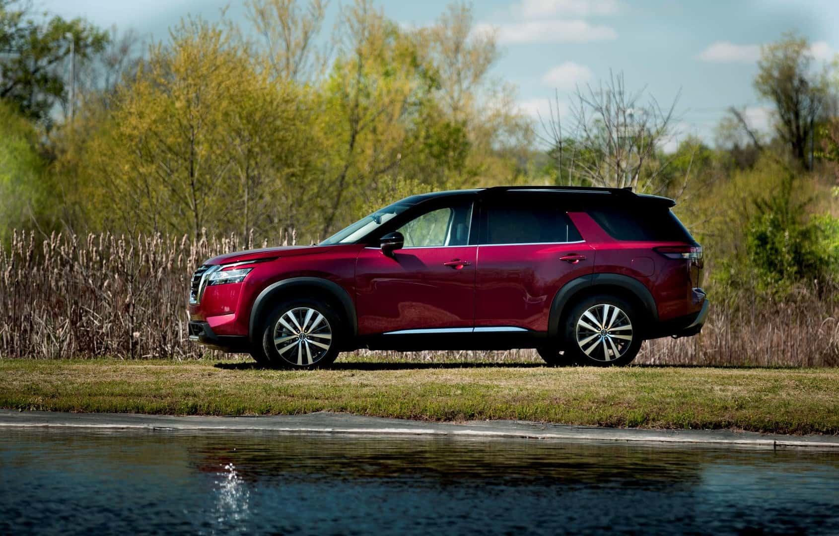 The Lipstick Red Side Profile Of The Award Winning Nissan Pathfinder, Parked Near A Shimmering Lake