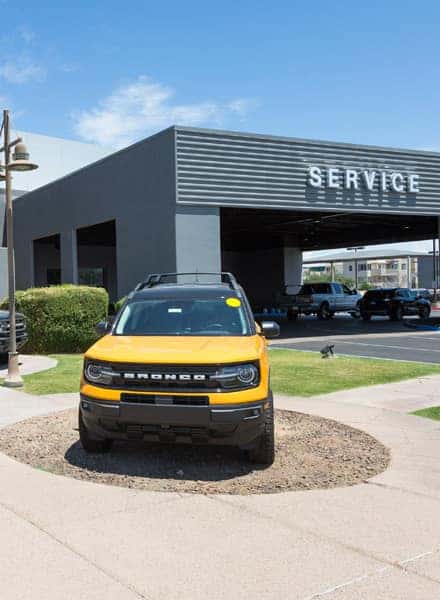 A yellow Ford Bronco is parked in front of the service department at Earnhardt Ford.