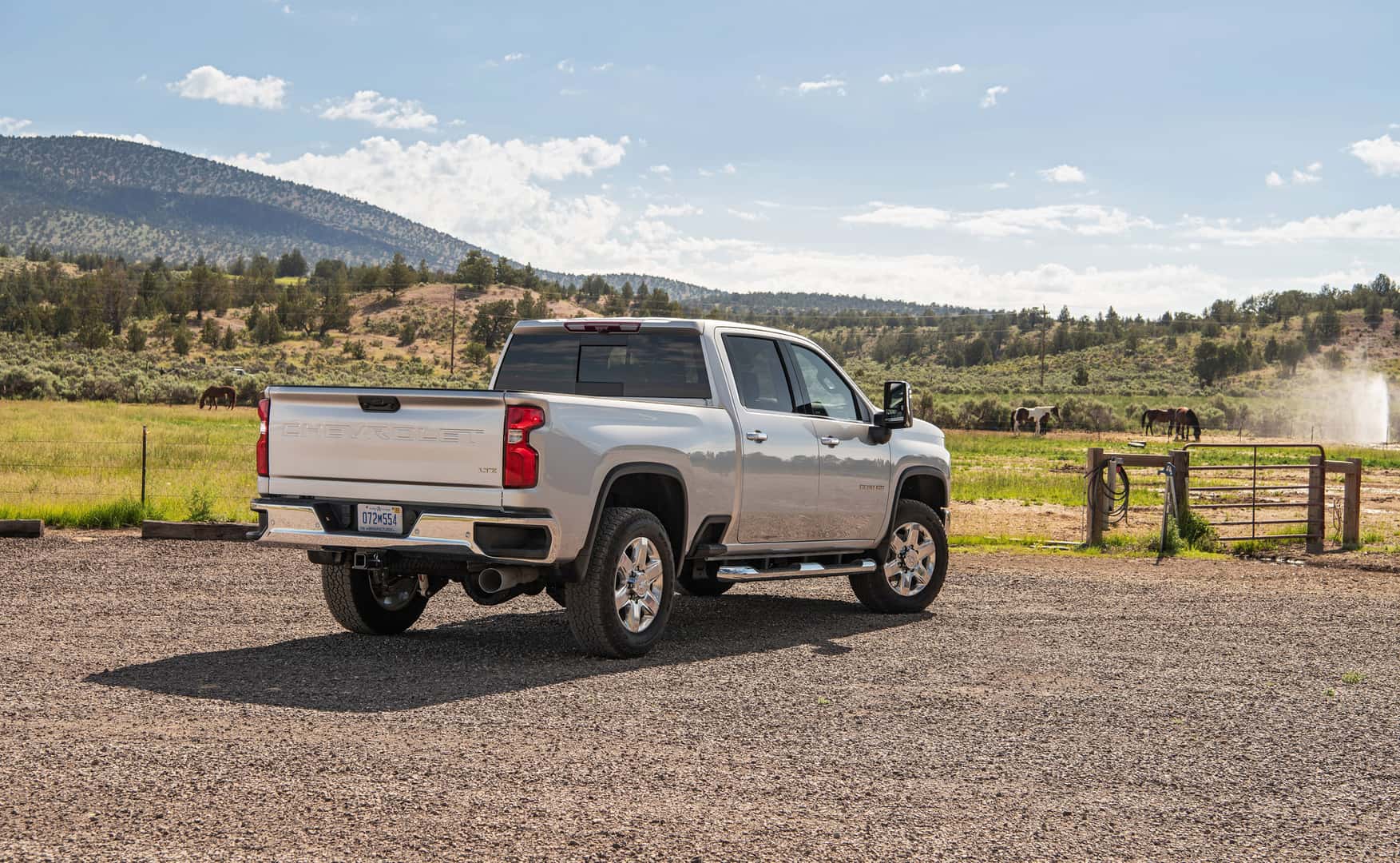 A white used Chevy Silverado 2500HD in Phoenix is parked facing away from the viewer to the right in a gravel lot in front of a horse pasture.