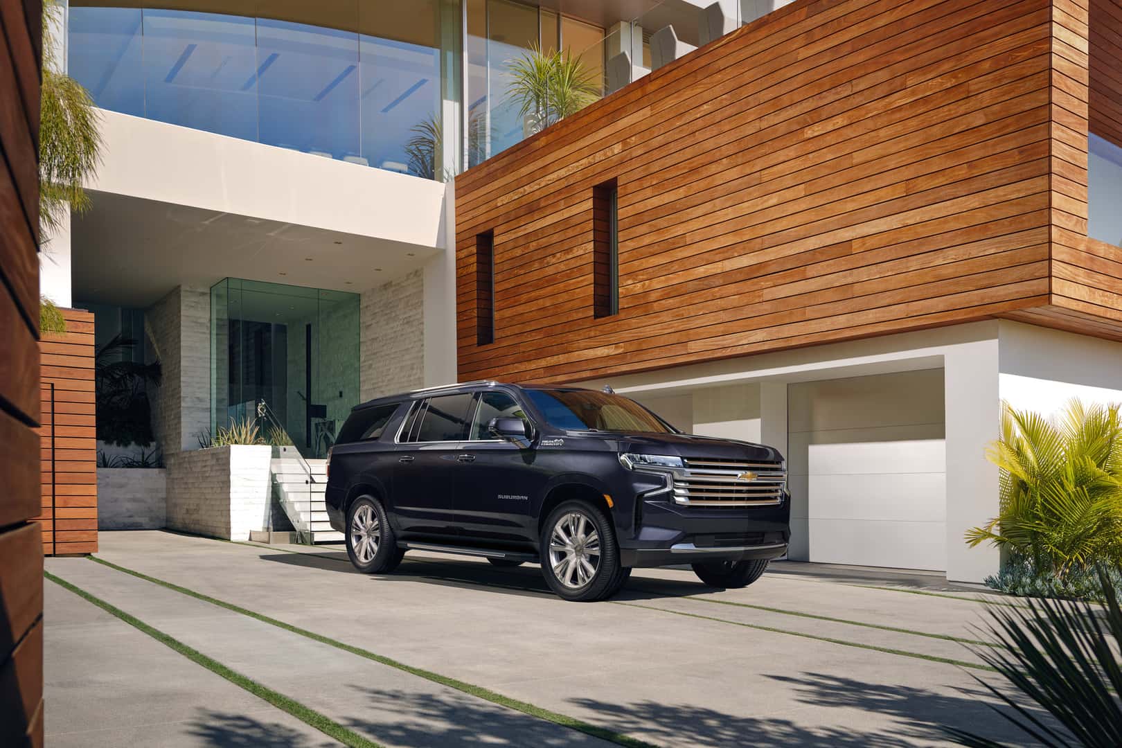A black used 2023 Chevy Suburban in Phoenix is parked facing the viewer to the right in a driveway in front of a modern house.