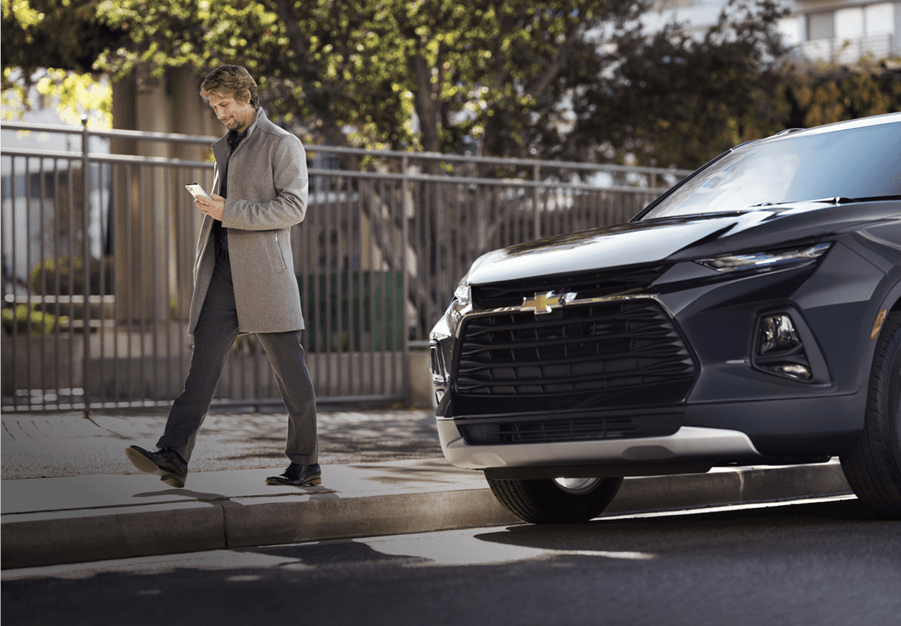 Man looking at his phone while walking past a parked Chevrolet