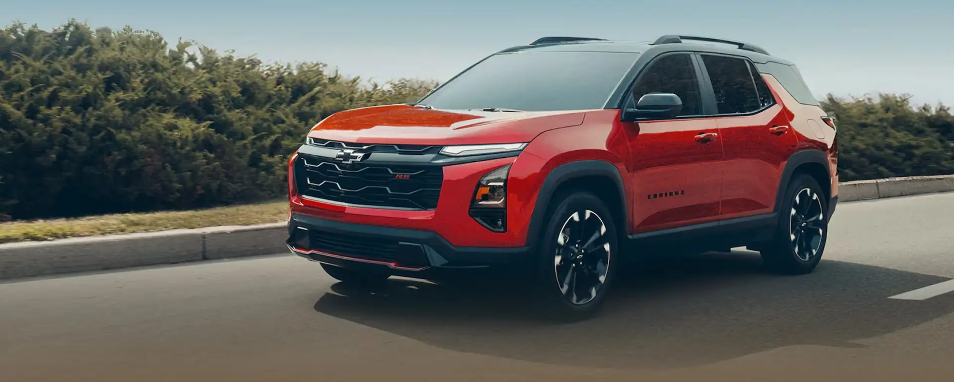 Red 2027 Chevrolet Equinox RS driving on a tree-lined road