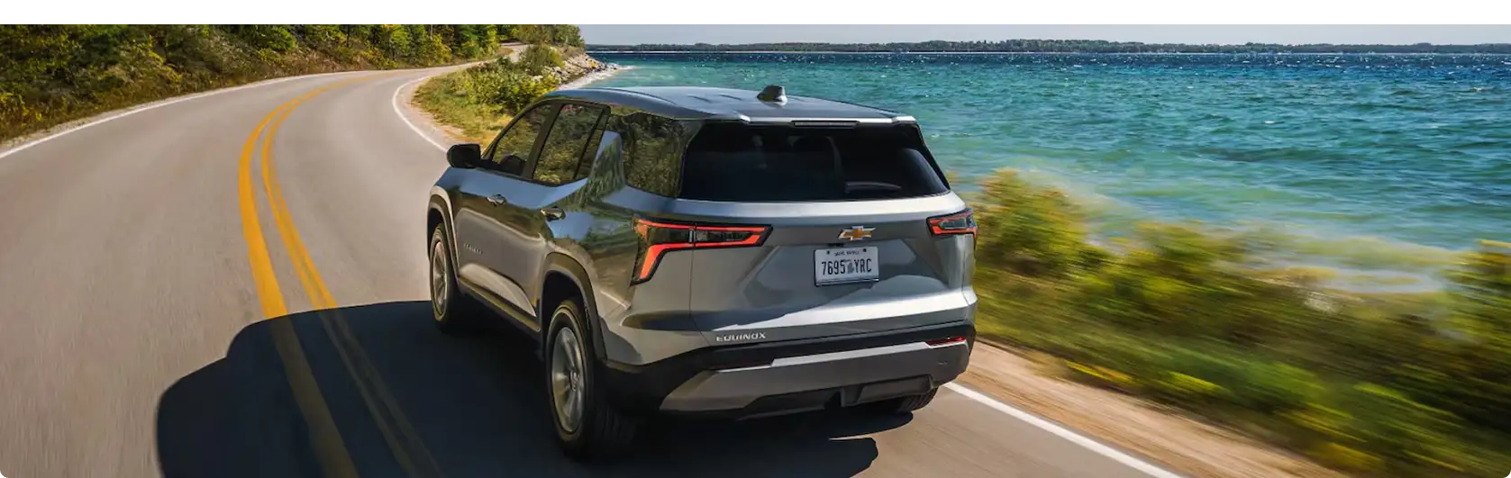 Silver 2027 Chevrolet Equinox driving on a coastal highway