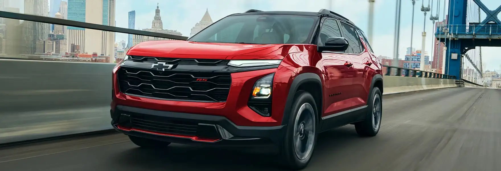 Red 2027 Chevrolet Equinox RS driving across a bridge with a city skyline behind